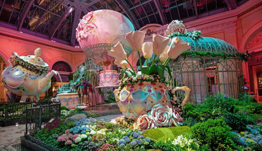 Bellagio Conservatory Display at night. Visible in the image is a large teapot with flowers, a floral hot air balloon being suspended in air, and a giant floral teapot pouring water into a teacup