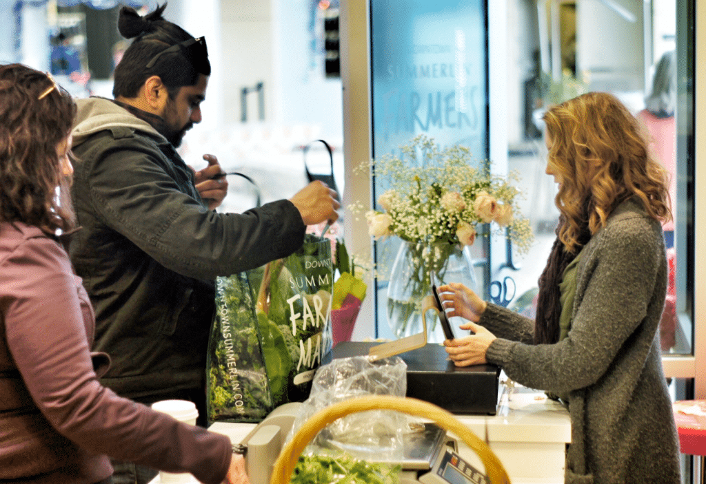 Man opening back that says Downtown Summerlin Farmers Market   while cashier rings him up at Intuitive Forager Farmers Market