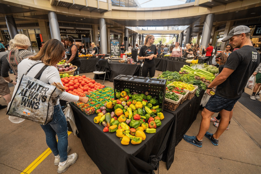 Group of people shopping at a farmers market booth with a large variety of vegetables at Las Vegas Farmers Market in Downtown Summerlin